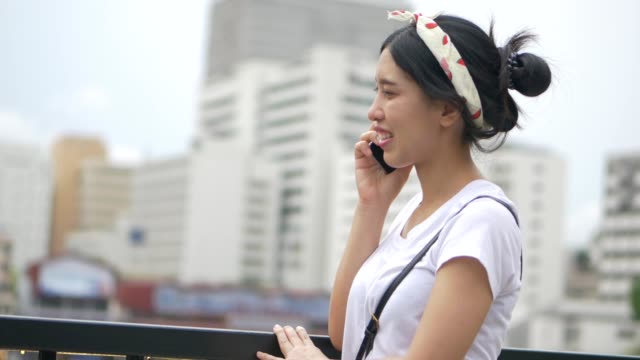 Schöne-junge-asiatische-Frau-im-Gespräch-auf-Smartphone-genießen-neben-Zaun-am-Fluss.