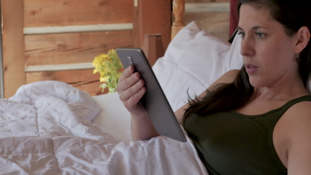 Frau-liest-ein-digitales-Tablet-und-trinkt-aus-einer-Kaffeetasse-in-ihrem-Bett