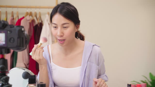 Beauty-blogger-present-beauty-cosmetics-sitting-in-front-camera-for-recording-video.-Happy-beautiful-young-Asian-woman-use-cosmetics-review-make-up-tutorial-broadcast-live-video-to-social-network.