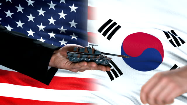 USA-and-South-Korea-officials-exchanging-tank-for-money,-flag-background,-deal