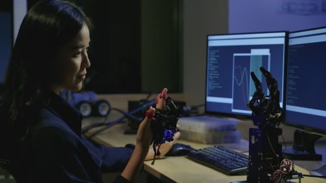 Junge-Elektronik-Entwicklungsingenieure-testen-innovative-Robotertechnologie-im-Labor.-Junge-asiatische-Frau-schafft-Bewegung-für-mechanische-Roboterhand.-Menschen-mit-Technologie--oder-Innovationskonzept.