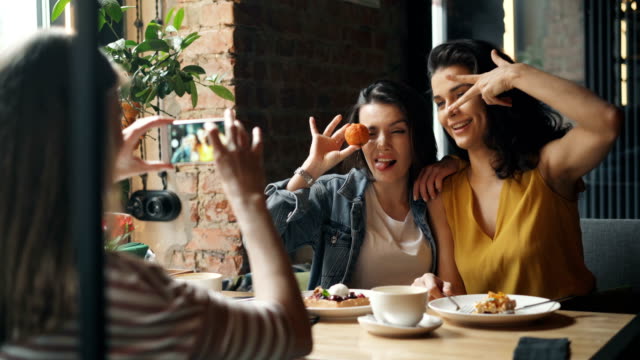 Attractive-young-ladies-taking-photos-in-cafe-posing-for-smartphone-camera