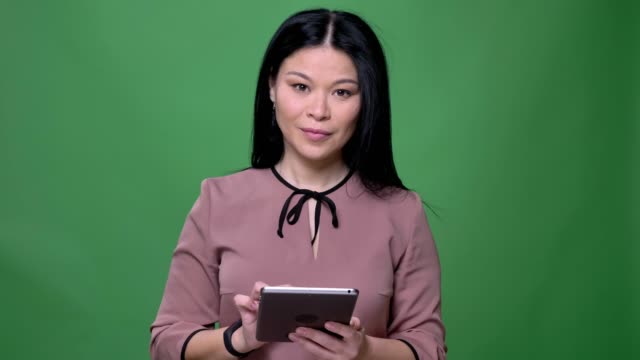 Nahaufnahme-von-jungen-attraktiven-asiatischen-Frau-mit-schwarzen-Haaren-SMS-auf-dem-Tablet-mit-Hintergrund-isoliert-auf-grün