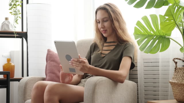 Chica-adolescente-feliz-usando-tableta-digital-en-el-sillón