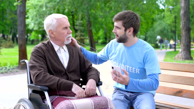 Positive-männliche-Freiwillige-unterhalten-behinderten-Patienten,-hören-gemeinsam-Musik