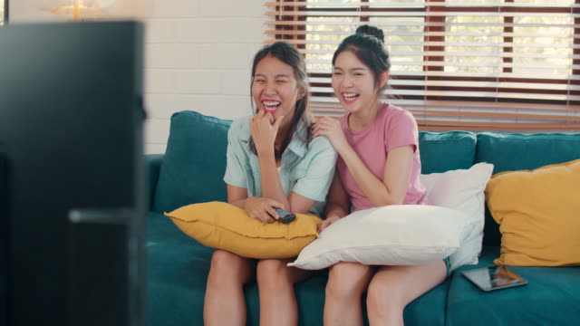 Joven-pareja-lesbiana-asiática-viendo-la-televisión-juntos-mientras-se-acuesta-sofá-en-la-sala-de-estar.