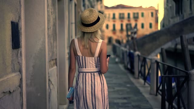 Attractive-caucasian-female-tourist-in-stylish-hat-searching-architect-building-during-walk-on-Venice