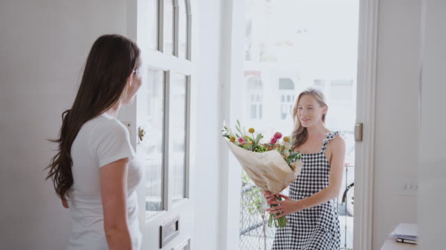 Frau-öffnet-Haustür-zu-Homosexuell-Partner-zu-Hause,-die-ihr-Bündel-von-Blumen-gibt
