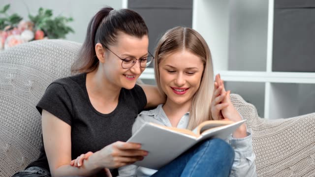 Zwei-lächelnde-homosexuelle-junge-Frau-lesen-Buch-zusammen-auf-der-Couch-Gefühl-Liebe-und-Zärtlichkeit