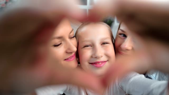 Close-up-face-happy-child-girl-showing-heart-gesture-by-hand-posing-two-lesbian-kissing-mother