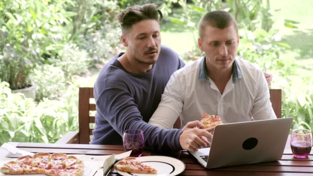 Gay-couple-having-pizza-for-lunch.-Browsing-and-eating-pizza.