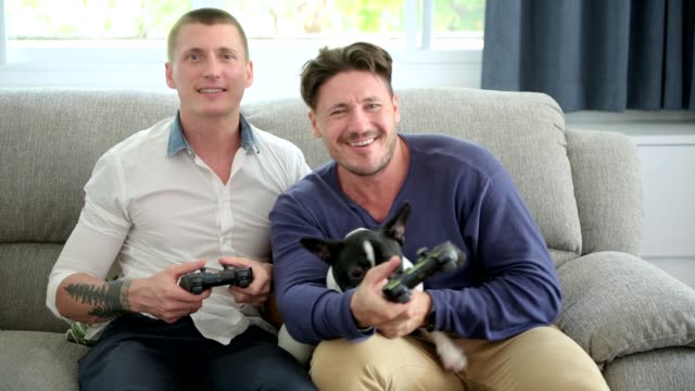 Gay-couple-relaxing-on-couch-with-dog-playing-games.-Playing-game.