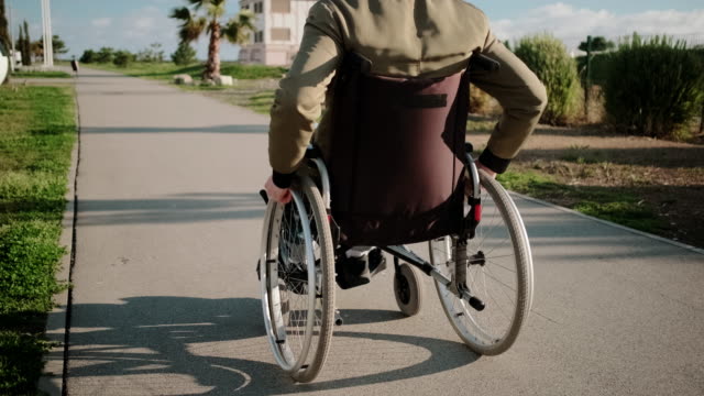 Walk-of-man-in-wheelchair-in-sunny-day-outdoors,-back-view
