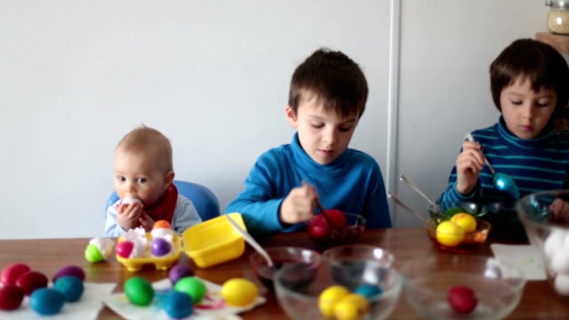 Three-children,-coloring-and-painting-easter-eggs-at-home-for-the-holiday