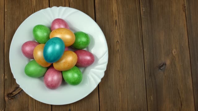 Una-persona-pone-huevos-de-pollo-multicolores-de-colores-en-un-plato,-fondo-de-madera,-vacaciones-de-Pascua,-espacio-de-copia,-casero