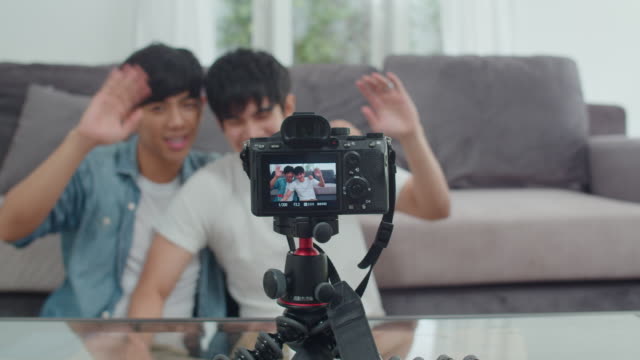 Young-Asian-gay-couple-influencer-couple-vlog-at-home.-Teen-korean-LGBTQ-men-happy-relax-fun-using-camera-record-vlog-video-upload-in-social-media-while-lying-sofa-in-living-room-at-house.-Slow-motion