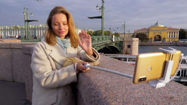 young-townswoman-is-taking-photo-by-smartphone-and-selfie-stick,-outdoors-on-bridge-in-city