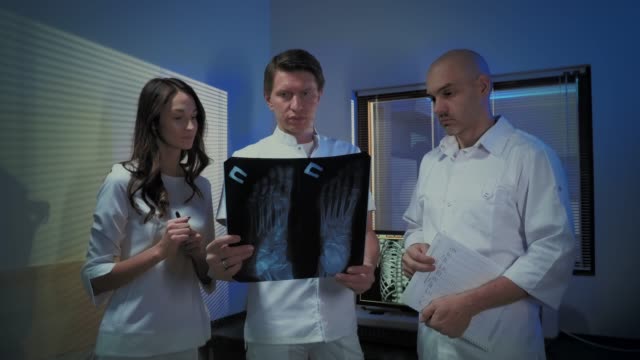 Tres-médicos-examinan-una-foto-de-rayos-X-de-un-paciente-juntos