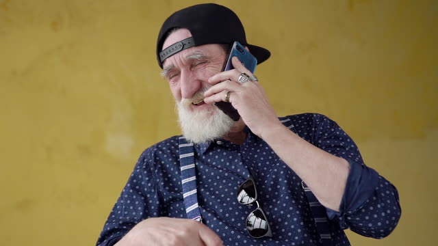 Front-view-of-happy-smiling-modern-bearded-senior-man-in-cap-which-having-phone-conversation-with-friend