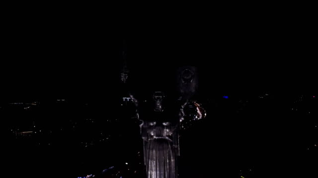 Vista-aérea-de-la-madre-patria-en-la-noche-con-las-luces-iluminadas,-el-monumento-se-encuentra-en-los-bancos-del-río-Dnieper.-Kiev,-Ucrania.-Rodada-en-4K-UHD