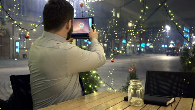 Empresario-toma-foto-por-aplicación-para-tablet,-en-la-noche,-en-café,-Navidad