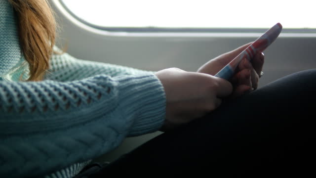 Young-girl-traveling-in-a-train-and-using-mobile-phone.-Beautiful-woman-sends-a-message-from-the-smartphone.-Attractive-girl-chatting-with-friends.