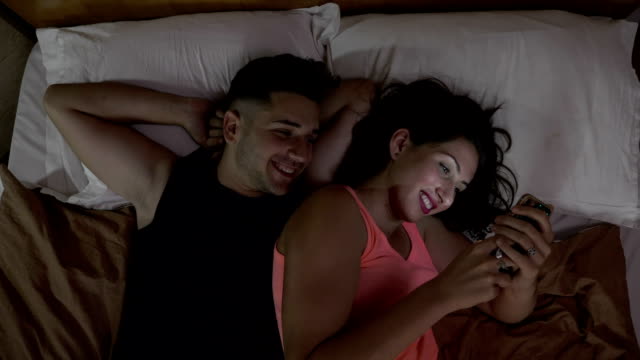 Glücklich-verheiratetes-Paar,-die-gerade-eines-lustigen-Videos-über-social-Media-auf-einem-Smartphone-auf-dem-Bett-zu-Hause