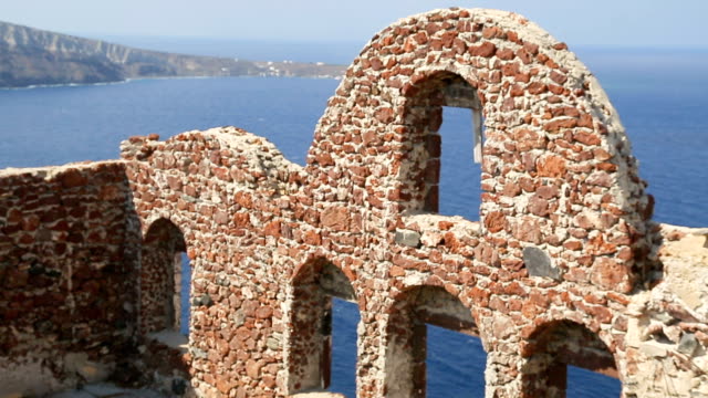 Remains-of-Oia-castle-against-blue-sea-on-Santorini,-stone-wall-with-cut-windows