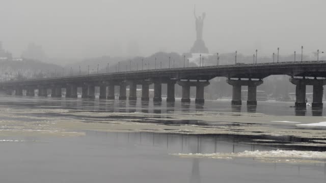 Blick-auf-die-Paton-Brücke-im-Winter.-Schneefall-in-Kiew-in-der-Nähe-des-Dnjepr.-Timelapse