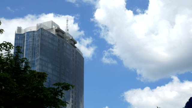 View-from-below-on-a-large-glass-business-center-against-a-background-of-moving-gray-clouds.-Reflection-in-glass