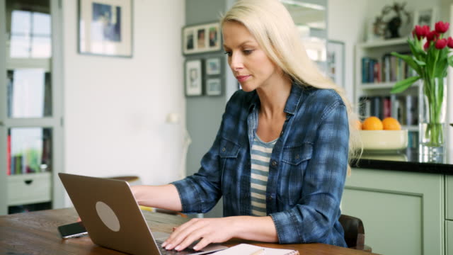 Schöne-blonde-Frau-auf-Laptop-tippen-und-mit-Smartphone