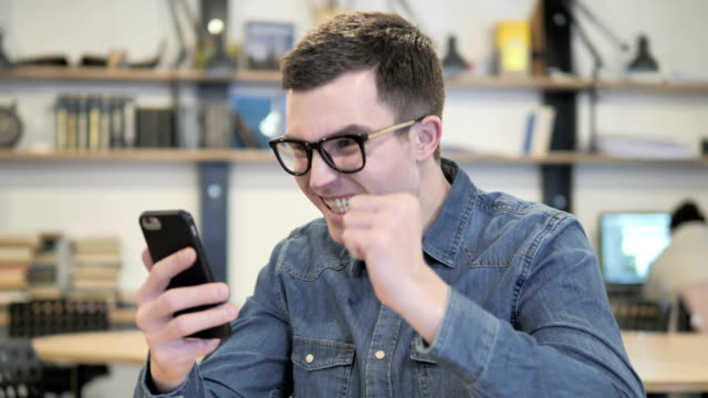 Excited-Young-Man-Enjoying-Success-while-Using-Smartphone