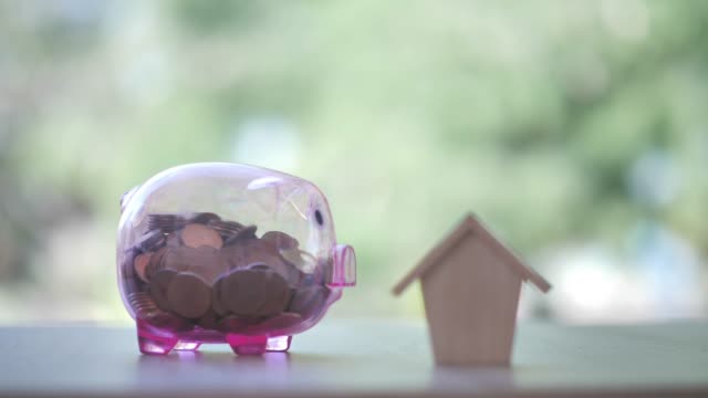 Hand-putting-money-coin-with-Piggy-bank-and-house-on-nature-background.-Property-investment-and-house-mortgage-financial,-Credit-home,-saving-concept