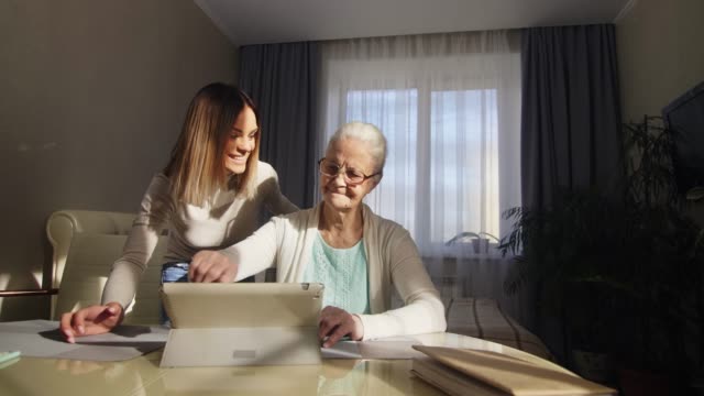 Senior-Woman-Learning-Tablet-mit-Hilfe-von-Adult-Granddaughter