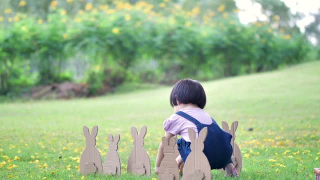 Cute-little-child-girl-on-Easter-day.-Girl-hunts-for-Easter-eggs-on-the-lawn-and-bunny-Made-of-paper-in-nature-or-park-and-sunlight.-Slow-Motion