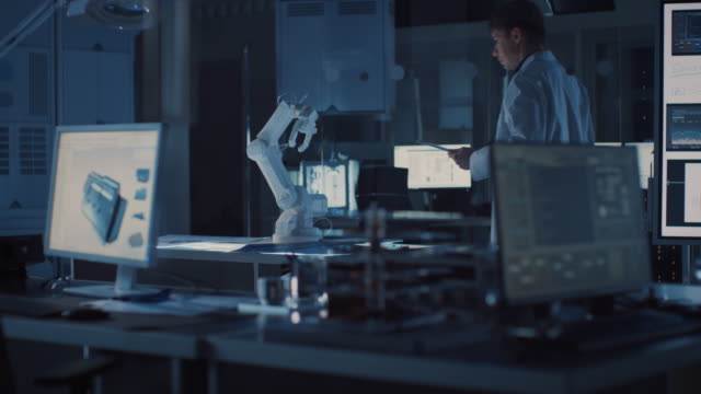 Professional-Heavy-Industry-Robotics-Engineer-Wearing-White-Coat-Holding-Tablet-Computer-Walks-Through-Laboratory.-Facility-Full-of-Computers,-Various-Industrial-Design-Components-and-with-Robotic-Arm