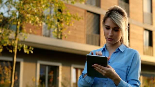 Portrait-of-young-girl-using-tablet-computer-in-the-park.-Modern-architecture-building-background