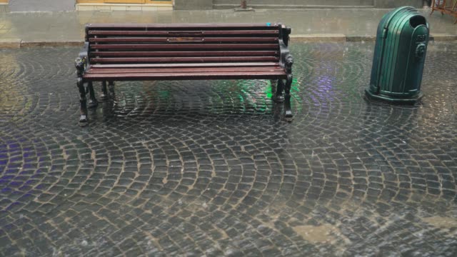 Heavy-rain-is-falling-on-the-pavement-and-modern-wooden-bench-outdoors-in-the-city.