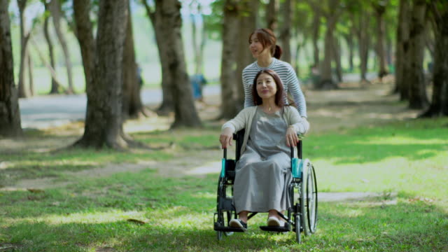 Hübsche-Teenager-Tochter-und-Mutter-auf-Rollstuhl-im-Park