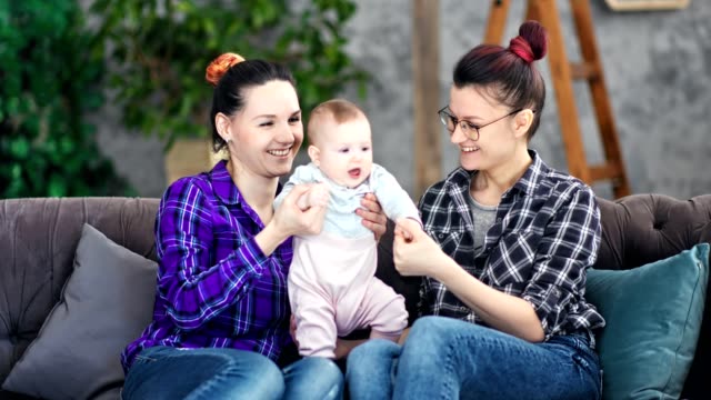 Zwei-lächelnde-junge-Mutter-genießen-Mutterschaft-spielen-mit-kleinen-niedlichen-Baby-in-gemütlichem-Haus