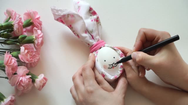 Women's-and-children's-hands-hold-chicken-egg-decorated-for-Easter-bunny-in-hands,-paint-rabbit's-face-with-marker.