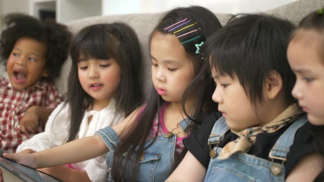 Grupo-de-niños-jugando-con-la-tableta-digital-juntos-en-el-sofá-en-casa,-y-sonriendo,-los-niños-en-la-tableta-digital-en-la-sala-de-estar.