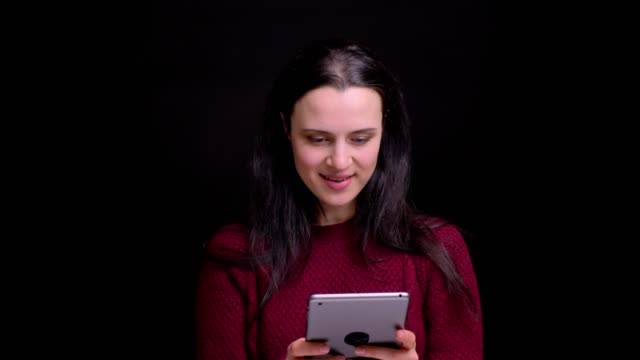 Closeup-portrait-of-young-caucasian-female-with-black-hair-color-using-the-tablet-and-laughing-with-background-isolated-on-black