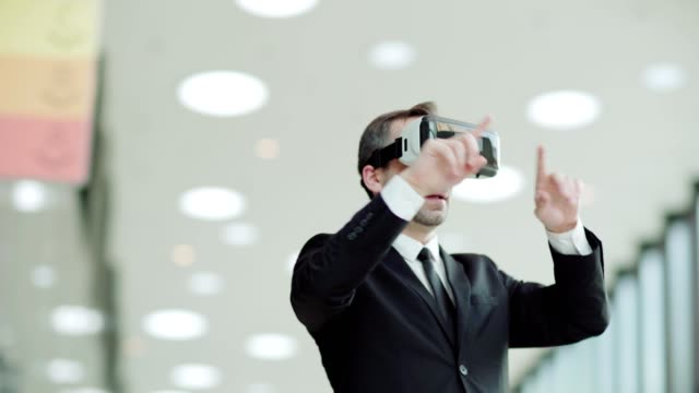 Toma-panorámica-del-Gerente-de-mediana-edad-en-traje-usando-gafas-de-realidad-virtual-y-explorando-datos-visualizados-de-pie-en-la-oficina