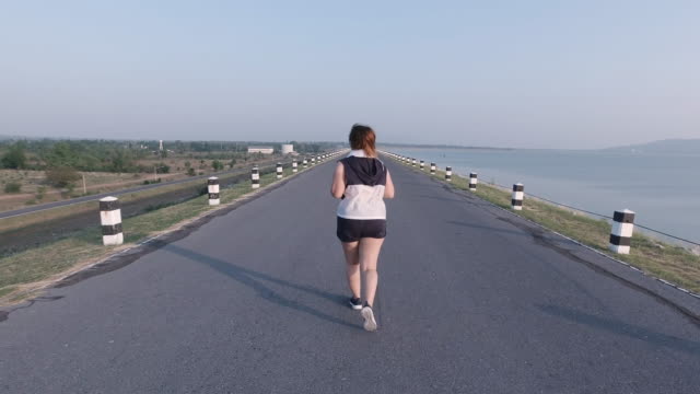 Asian-women-jogging-in-the-street-in-the-early-morning-sunlight-at-water-storage-Pa-Sak-Jolasid-Dam.-concept-of-losing-weight-with-exercise-for-health.-Slow-motion,-Rear-View