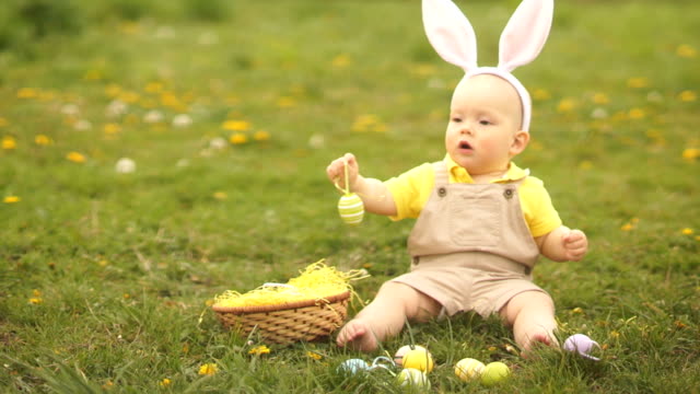 Lovely-baby-in-an-Easter-bunny-costume-collects-Easter-eggs-in-a-basket-sitting-on-the-grass-in-the-park.-Spring-picnic,-happy-easter-family