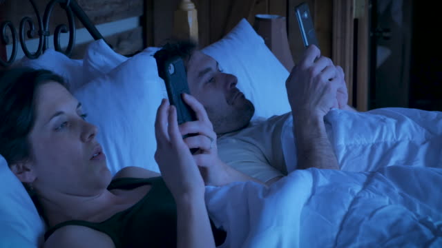 Man-and-woman-lying-in-bed-looking-at-their-mobile-phones-at-night