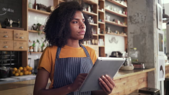 Thoughtful-female-cafe-owner-using-digital-tablet