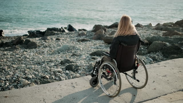 Una-mujer-discapacitada-está-sentada-en-silla-de-ruedas-cerca-de-la-orilla-del-mar-y-observando-olas
