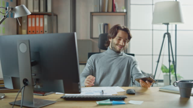 Handsome-Long-Haired-Entrepreneur-Sitting-at-His-Desk-in-the-Office-Works-on-Desktop-Computer,-Working-with-Documents,-Correcting-Charts,-Drawing-Graphs